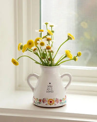 White ceramic artisan bud vase with floral designs holding yellow and white daisies