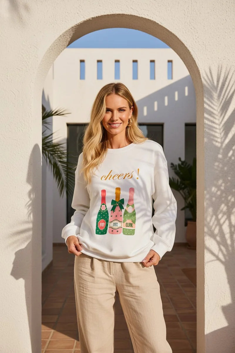 White Cheers graphic sweatshirt with colorful champagne bottle and beige pants