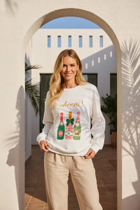 White Cheers graphic sweatshirt with colorful champagne bottle and beige pants