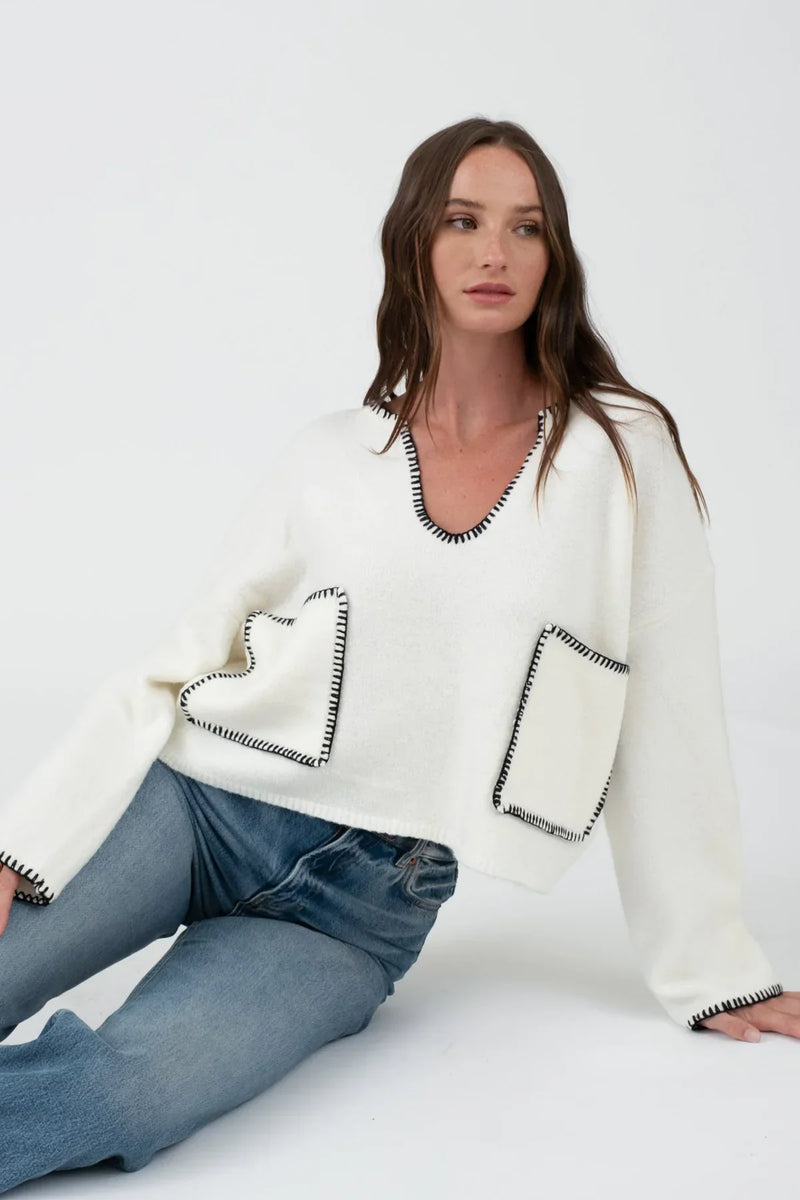 White knit sweater with black trim and pocket details, ideal for women’s boho chic clothing