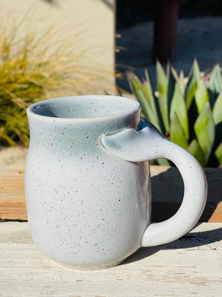 White stoneware mug with a whale tail handle placed on a wooden table