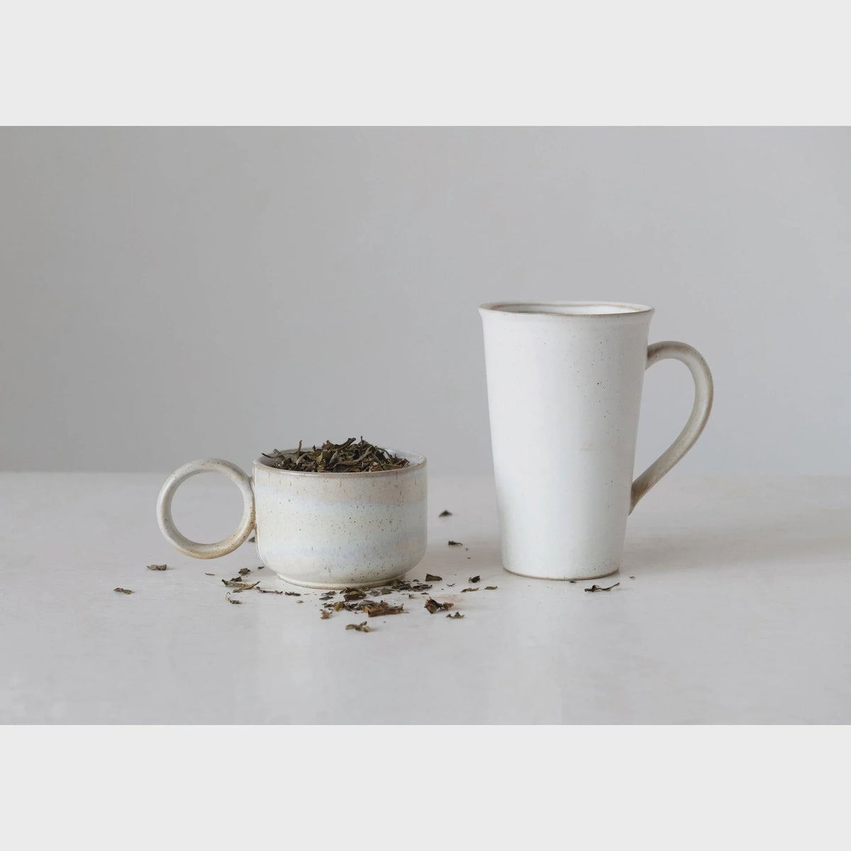 White stoneware mug with reactive glaze and a small pile of tea leaves inside