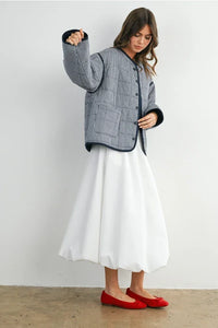 Buttoned quilted puffer jacket with white pleated skirt and red ballet flats