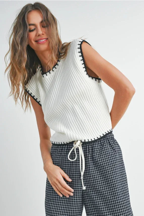 White ribbed knit sleeveless sweater vest with black whipstitch trim and drawstring hem