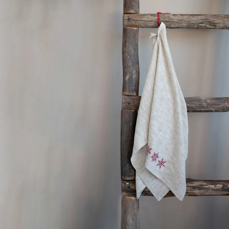 White cotton embroidered tea towel with pink floral design on wooden ladder