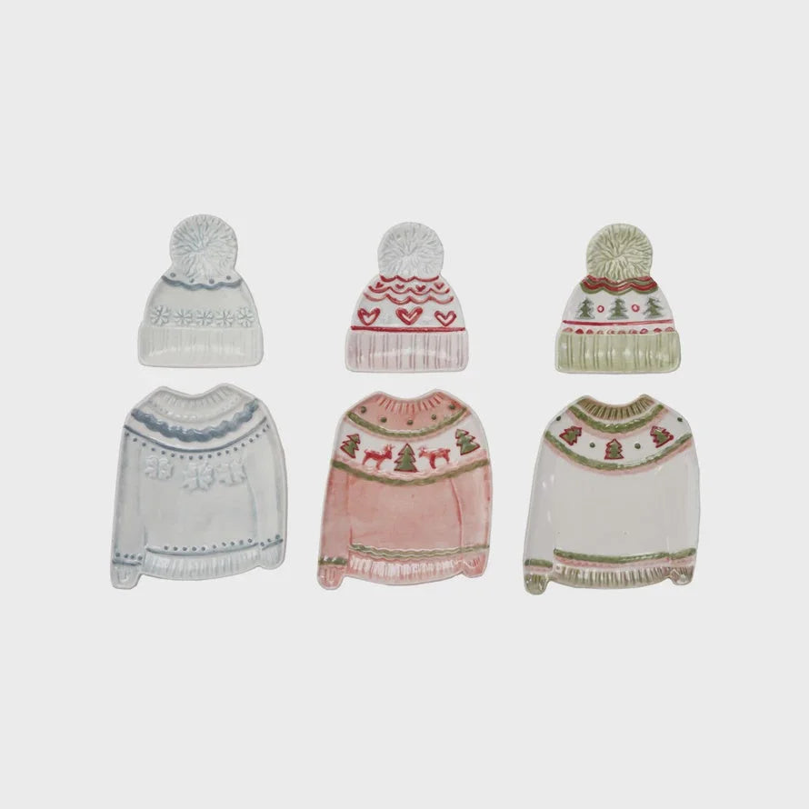 Winter-themed knit beanie set with pom-poms and holiday patterns on a sweater shaped plate