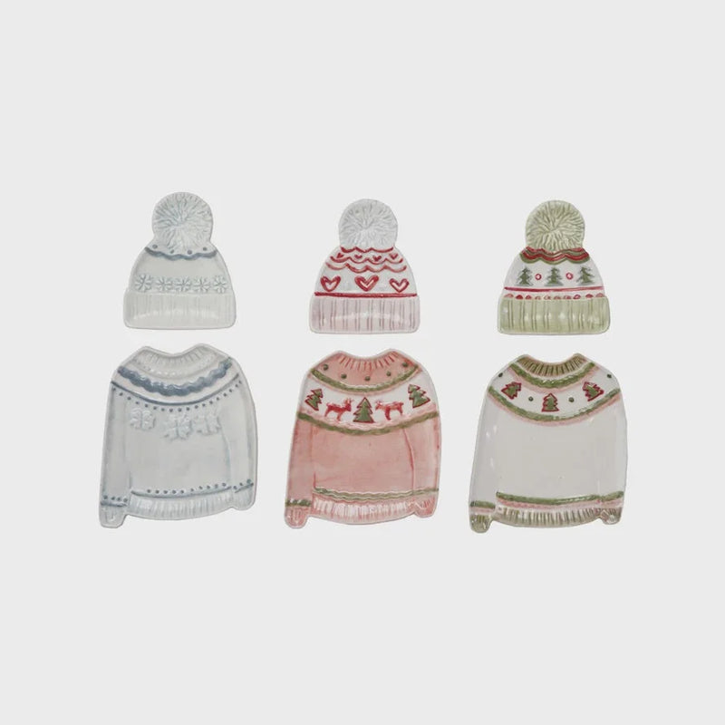 Winter-themed knit beanie set with pom-poms and holiday patterns on a sweater shaped plate