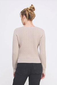 Woman wearing beige cable-knit pullover sweater with scallop v-neck detail and black jeans