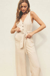 Woman in a beige BUTTON DOWN SASH BELT JUMPSUIT featuring v-neck button closures