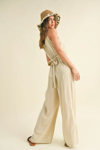 Woman in a beige DYE & WASH JUMPSUIT with floral hat, showcasing boho style