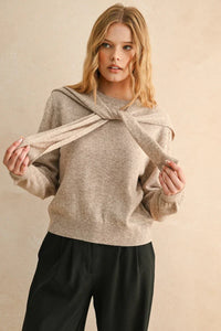 Woman wearing beige knit round neck sweater with matching scarf and black trousers