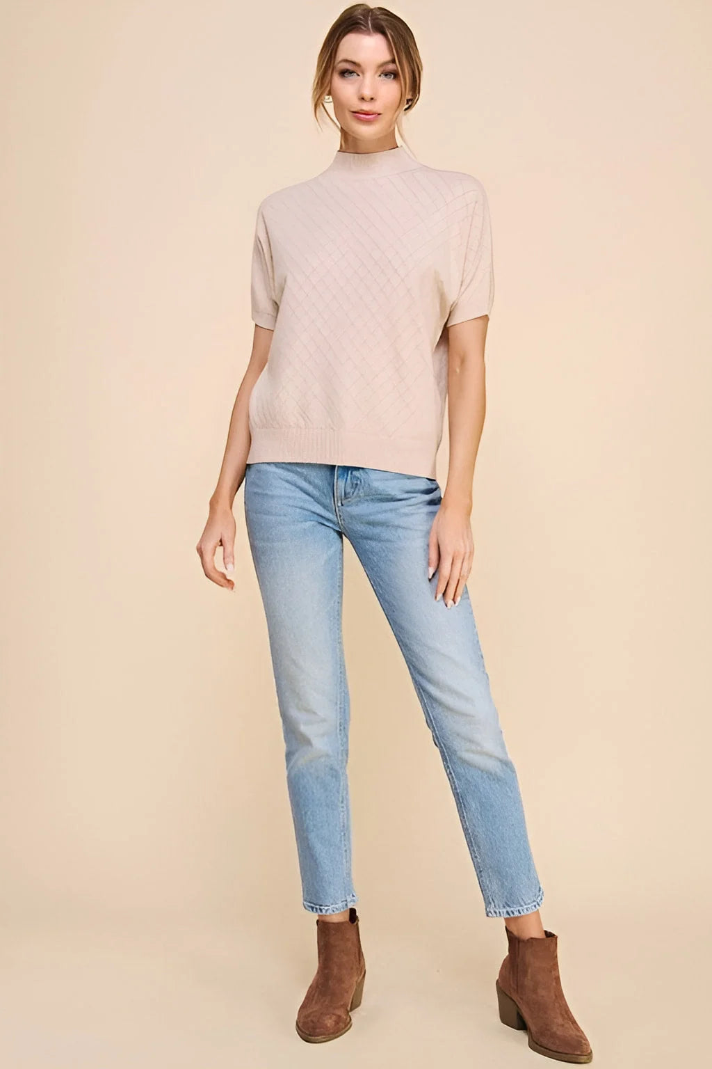 Woman in soft short sleeve crosshatch mock neck top, light blue jeans, and brown boots