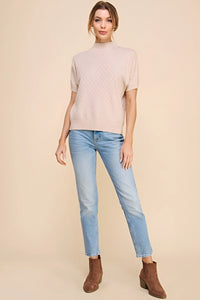 Woman in soft short sleeve crosshatch mock neck top, light blue jeans, and brown boots