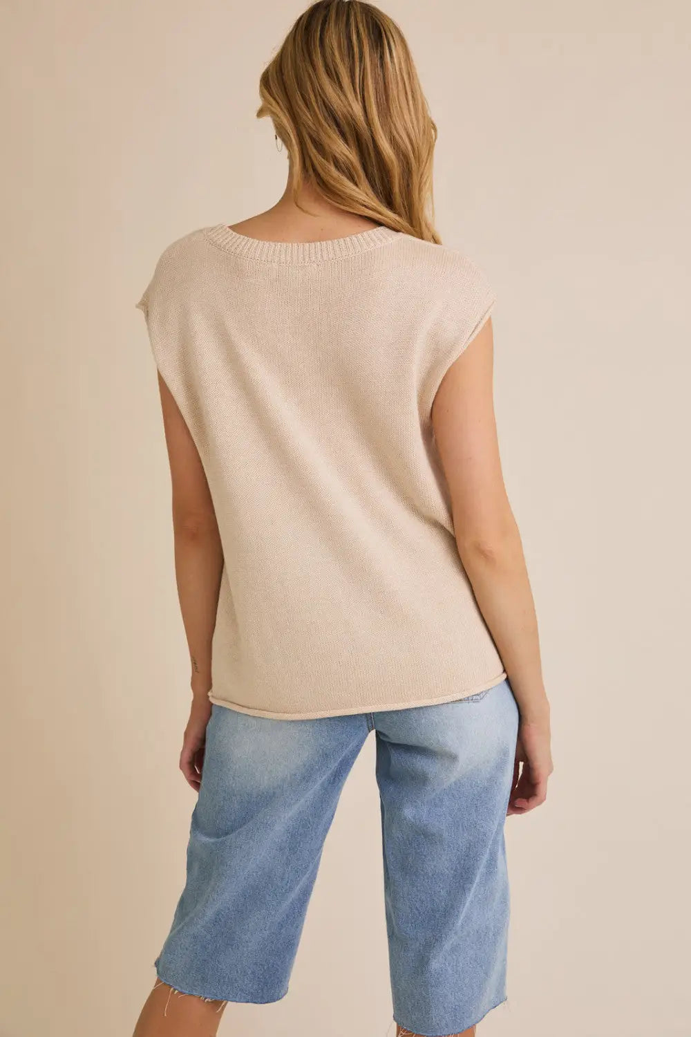 Woman wearing beige sleeveless top with wide shoulder USA flag sweater featuring shoulder USA flag design