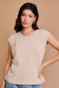 Woman in a beige sleeveless round neck top with pleated shoulder and blue jeans