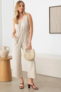 Woman in a beige wide leg sleeveless jumpsuit with a woven handbag for a boho look