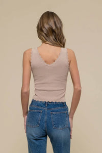 Woman in beige scallop edge sleeveless crop top and blue jeans, viewed from behind