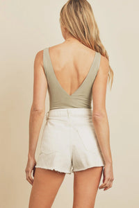 Woman in a beige top and white shorts showcasing the double plunging bodysuit