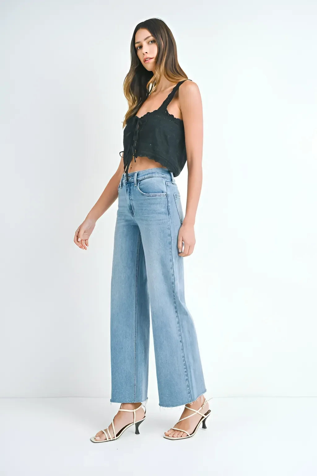 Woman in a black crop top and light blue long wide leg denim jeans with heeled sandals