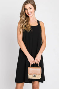 Woman in a black solid spaghetti strap dress with a stylish straw bag