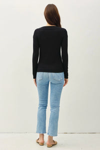 Woman wearing a basic boat neck long sleeve knit top with a fitted silhouette and light-wash jeans