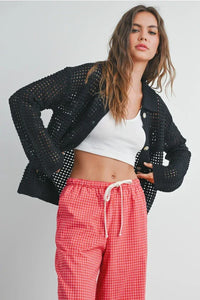 Woman modeling open stitch crochet black mesh button-up shirt with white crop top and red checkered pants