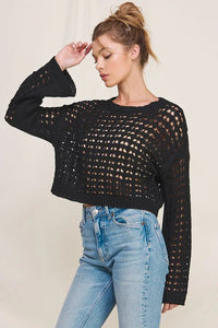 Woman wearing a long flared sleeve open weave sweater with a cropped fit and blue jeans