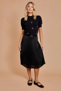 Woman in a black pleated skirt and embellished MOCK NECK HALF SLEEVE MARTINI top from Shop Daisy