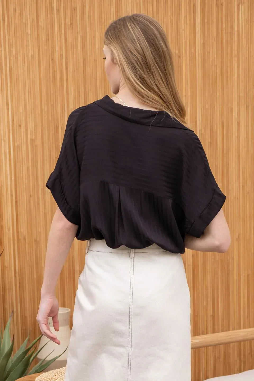 Woman in a striped collared split neck blouse, black top and white skirt, viewed from behind