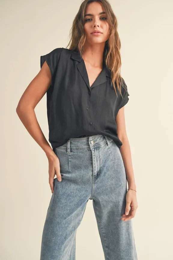 Woman modeling a black cap sleeve shirt with light blue jeans in a stylish outfit