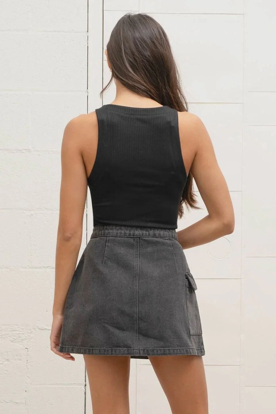 Woman in a black sweater knit tank top and gray denim skirt, viewed from behind