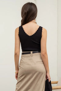 Woman in scallop edge sleeveless black top and beige skirt, viewed from behind