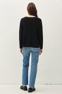 Woman in a black relaxed v-neck sweater with center seam and blue jeans, boho style