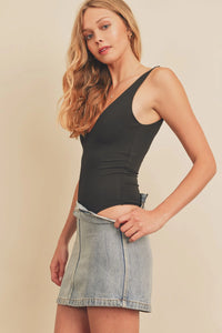 Woman in a black tank top and light denim skirt showcasing a double plunging bodysuit