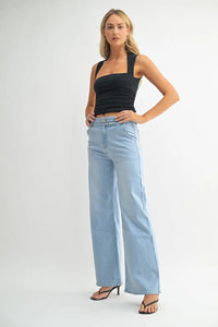 Woman in a black tank top and light blue denim belted wide leg jeans