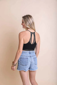 Woman in a black tank top and denim shorts showcasing a seamless polka dot lace trim bralette