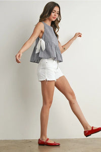 Woman wearing Sky Meadow Peplum Blouse in black and white gingham with white distressed shorts and red Mary Jane flats