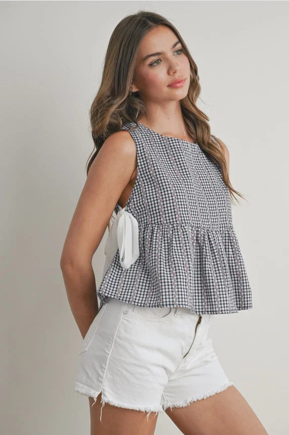 Woman wearing Sky Meadow Peplum blouse in black and white gingham with white shorts