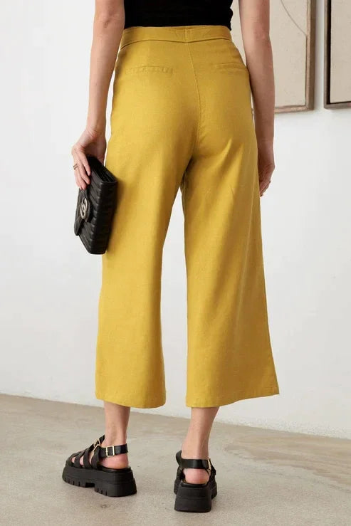 Woman wearing BELTED ASYMMETRIC WAISTBAND SNAP BUTTON PANTS in black top and yellow culots