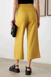 Woman wearing BELTED ASYMMETRIC WAISTBAND SNAP BUTTON PANTS in black top and yellow culots