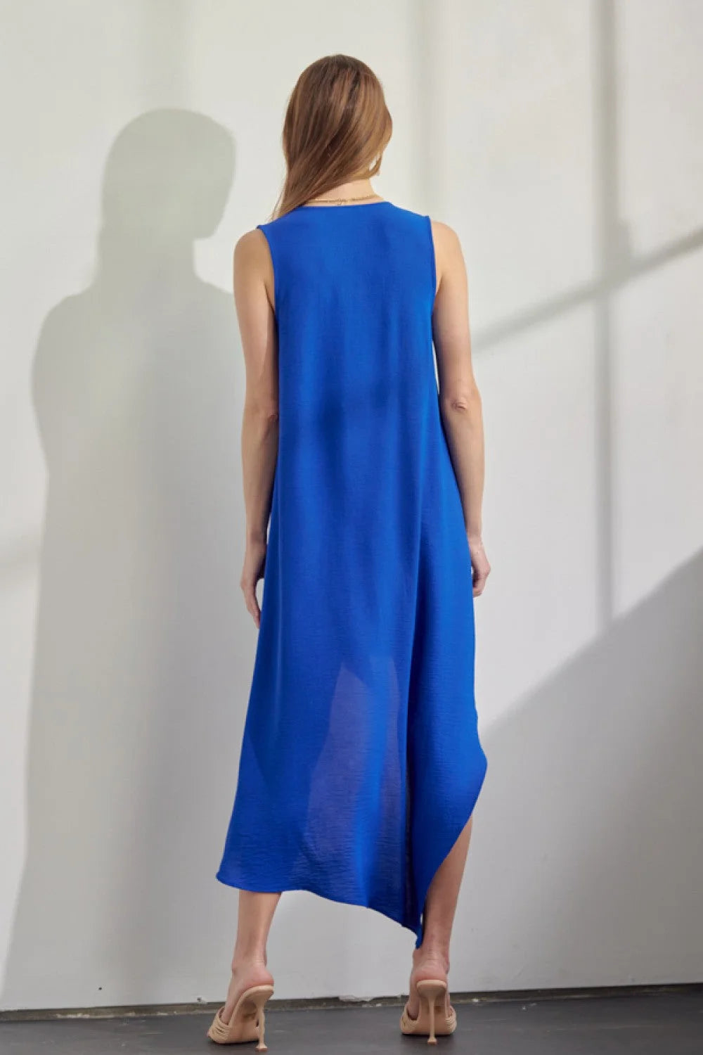 Woman in a blue low dress stands against a white wall, showcasing summer dresses for women