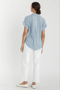 Woman in blue shirt and white pants wearing SOLID SHORT SLEEVE BUTTON DOWN SHIRT for women’s boho chic clothing from Shop Daisy
