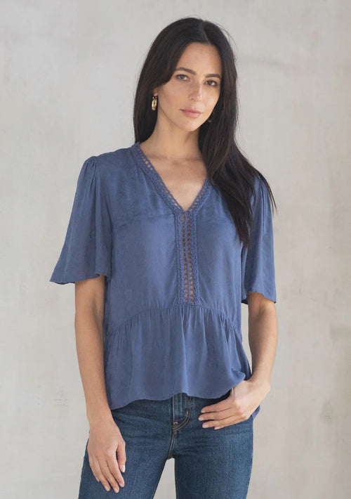 Woman modeling floral jacquard airy short sleeve peplum blouse with V-neck and dark jeans
