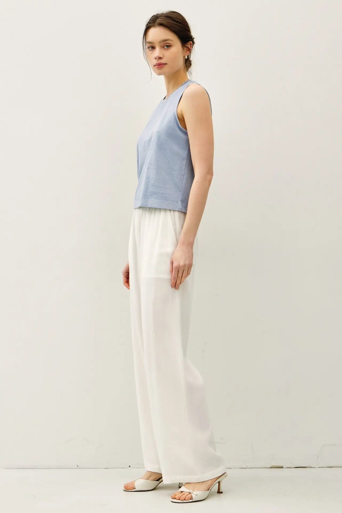 Woman wearing a blue acid wash boxy cut tank top and white pants