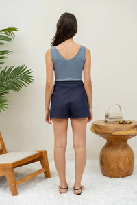 Woman in a blue scallop edge sleeveless top and navy shorts, viewed from behind