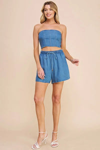 Woman in a blue strapless crop top and washed denim high waisted tie shorts