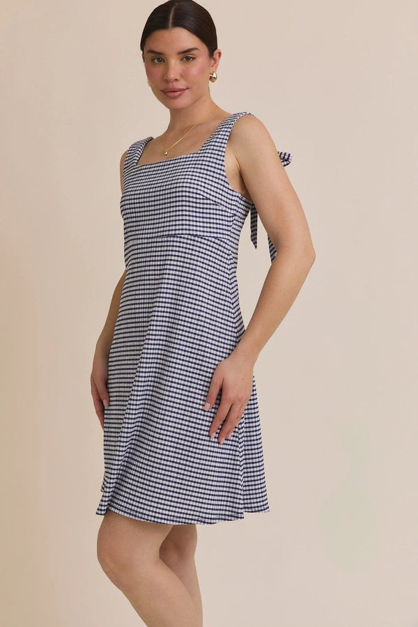 Woman wearing a blue and white gingham stripe sleeveless mini dress with shoulder ties