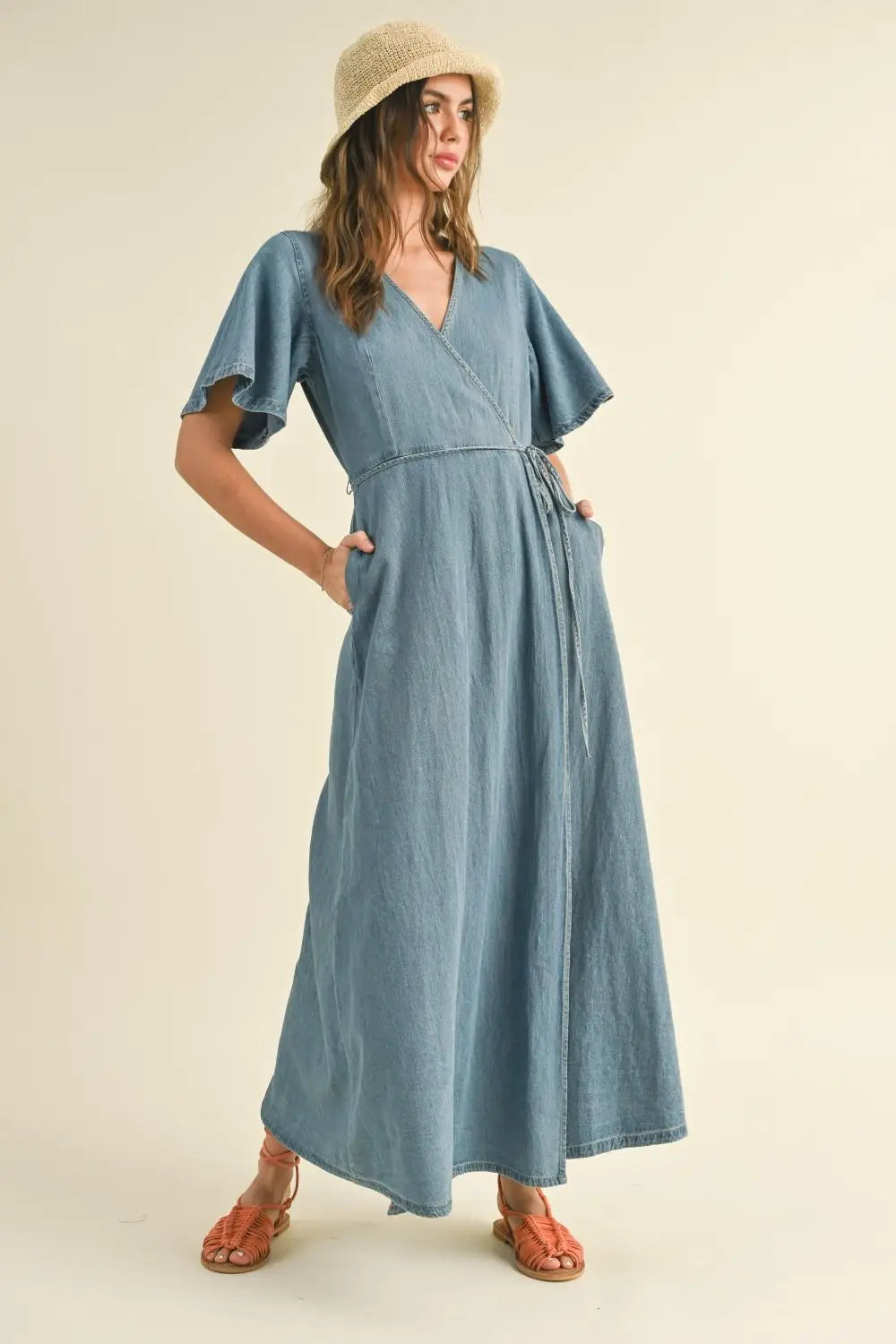 Woman in a blue washed denim wrap maxi dress and hat showcasing elegant style