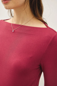 Woman wearing a deep red long sleeve knit top with a basic boat neck and fitted silhouette