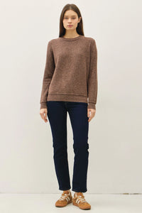 Woman modeling brown crew neck pullover with exposed seams, dark blue jeans, and tan sneakers